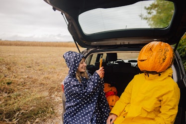 Photo of a smiling couple sitting in a car trunk and having fun after pumpkins picking.