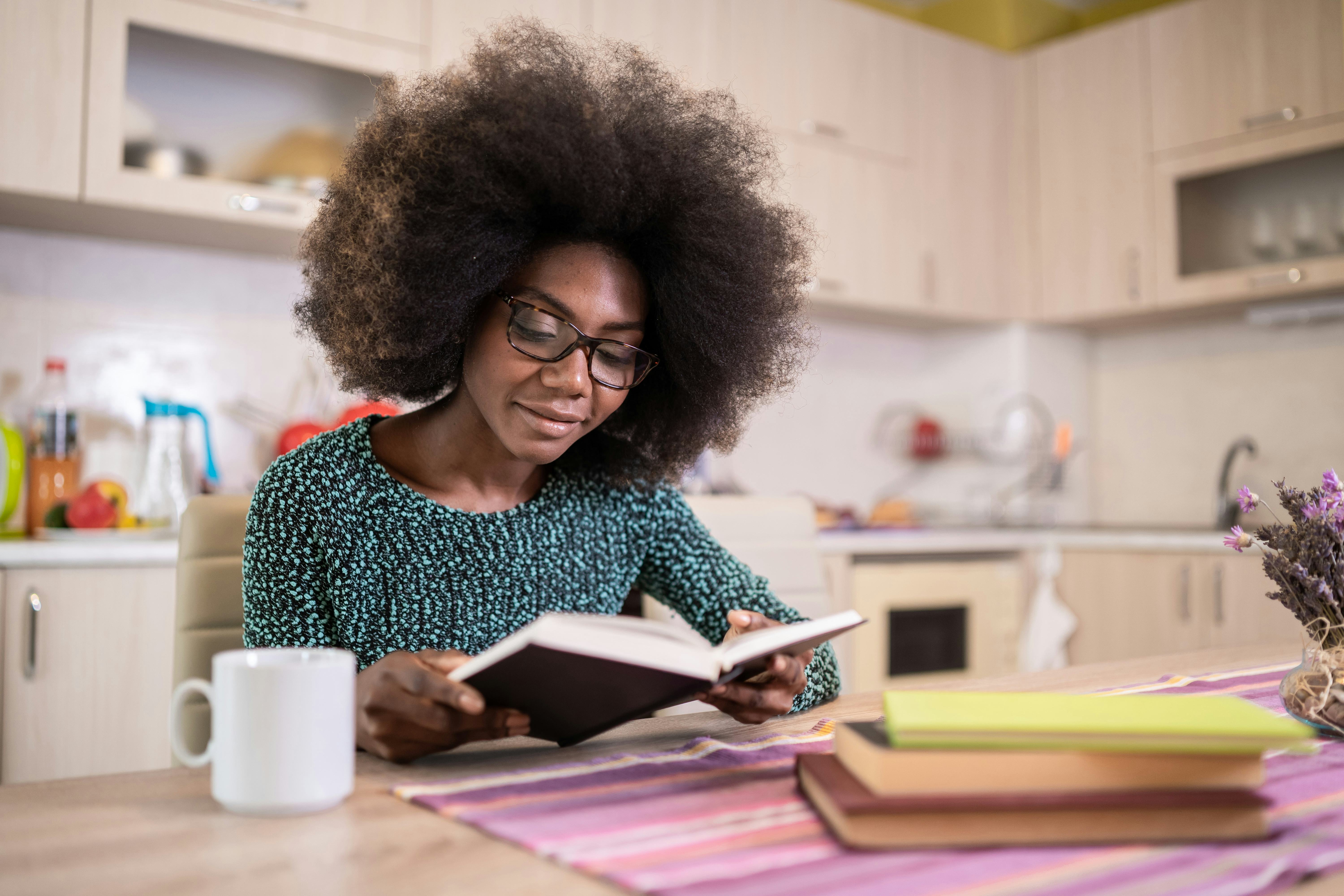 Portrait of attractive african american young woman sitting in the kitchen reading book