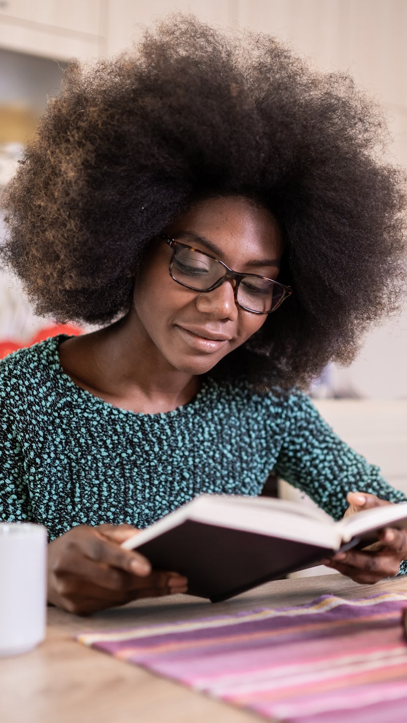Portrait of attractive african american young woman sitting in the kitchen reading book
