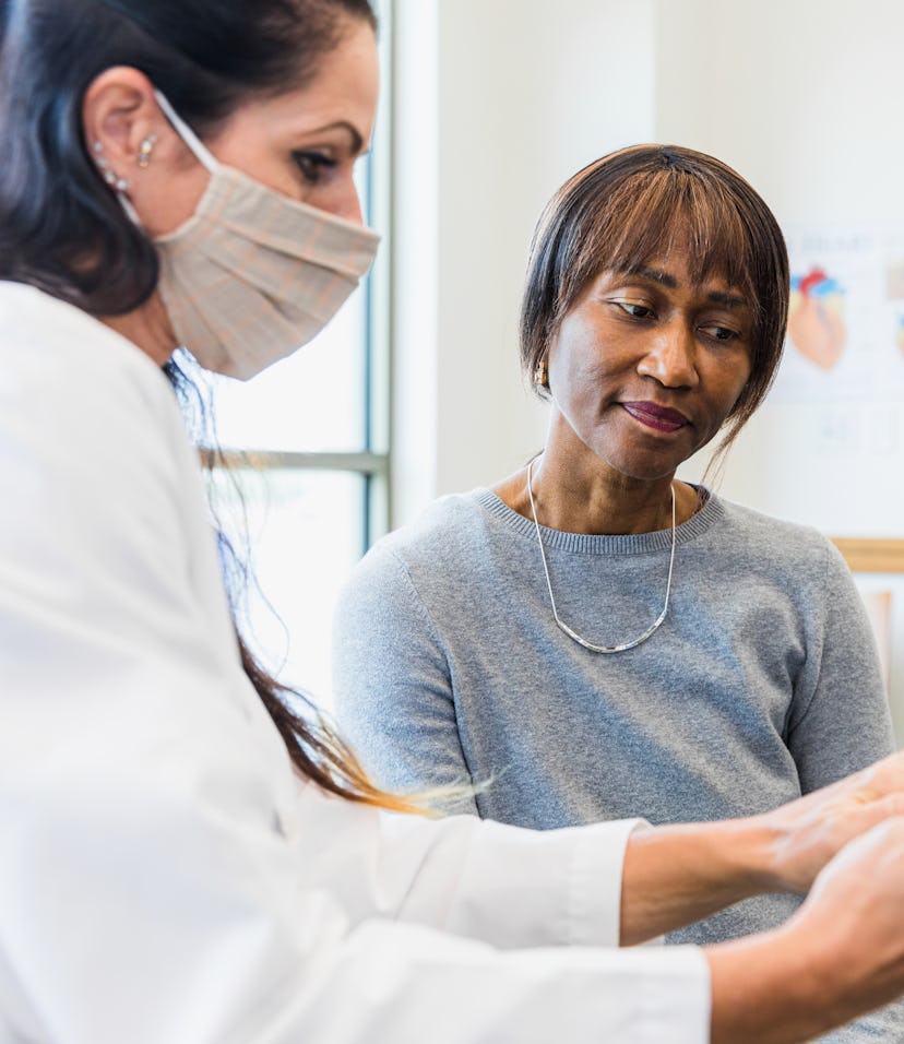 In order to protect her mature adult patient, the mid adult female doctor wears a protective mask wh...