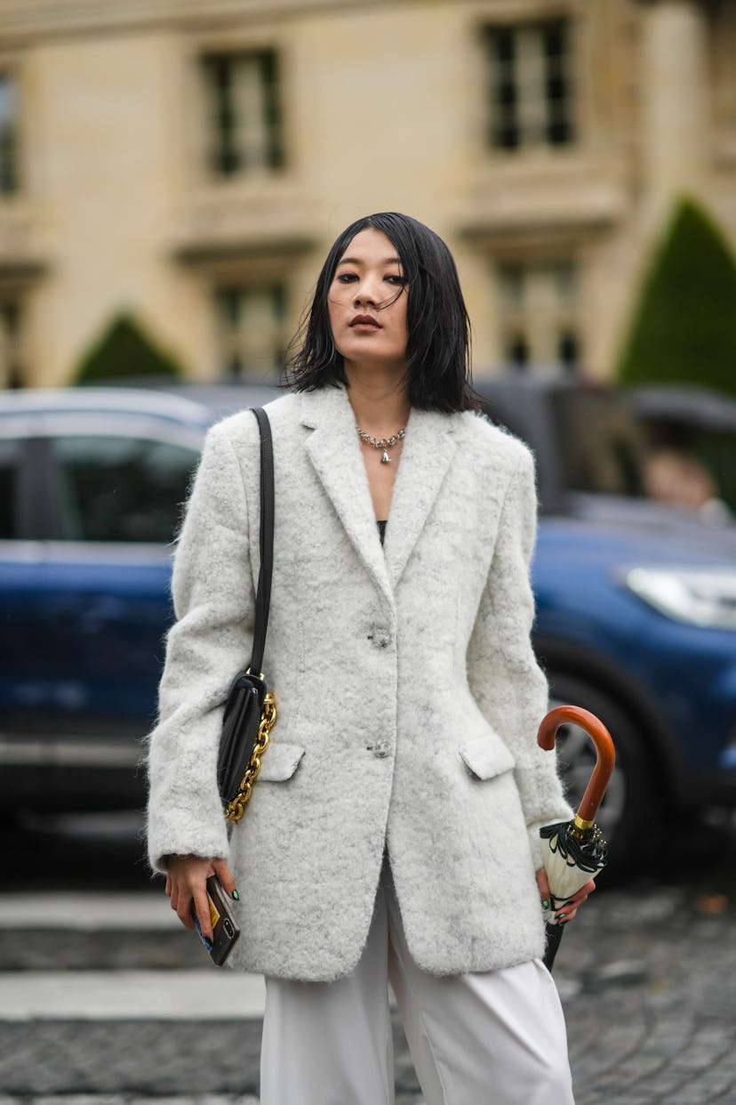 PARIS, FRANCE - OCTOBER 05: A guest wears a silver large chain pendant necklace, a white fluffy long...