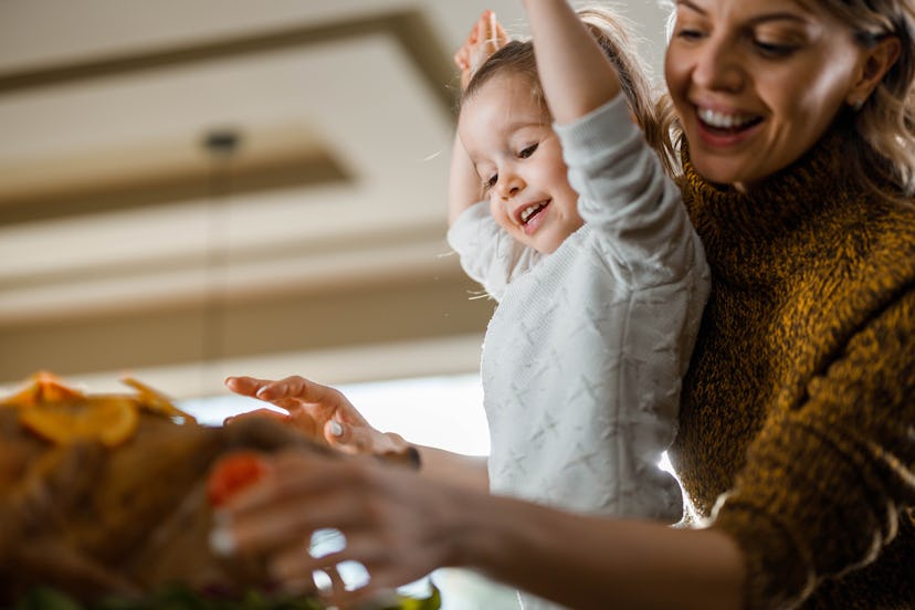 Young happy mother and her small daughter decorating Thanksgiving turkey in dining room. Focus is on...