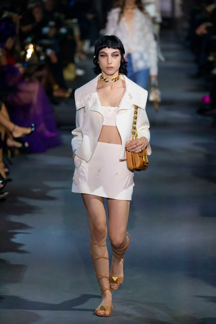 A model walking in a white jacket and skirt at the Valentino Ready to Wear Spring/Summer 2022 fashio...