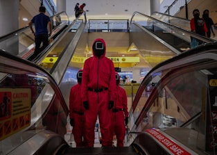 TOPSHOT - Cosplayers dressed in outfits from the Netflix series "Squid Game" ride an escalator at a ...