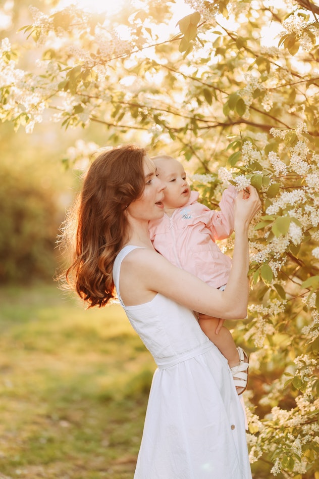 Image of women holding a young baby, picking petals off of a blooming tree.