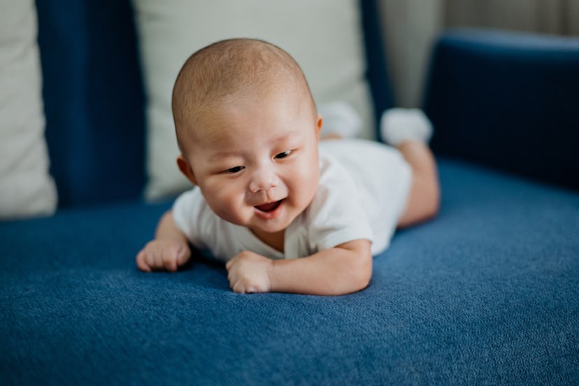 Image of a smiling Asian baby boy tummy time on sofa