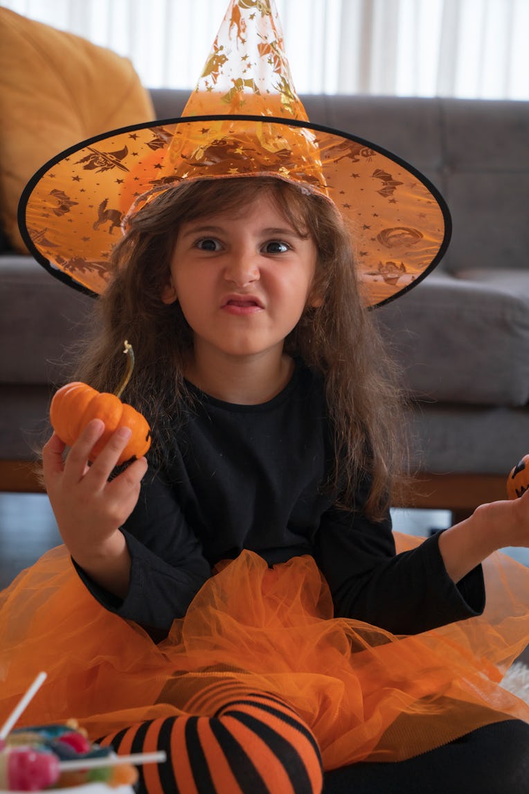 girl is playing at the Halloween party, covering their faces with Jack O'Lantern