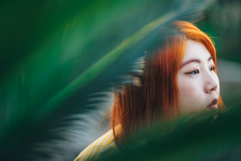 A woman with red hair looks out behind plants. These are Ophiuchus' biggest strengths, according to ...