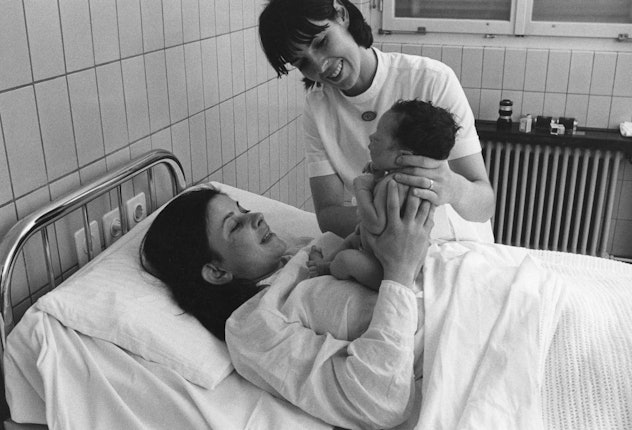 A midwife hands a new mom her baby in 1970.