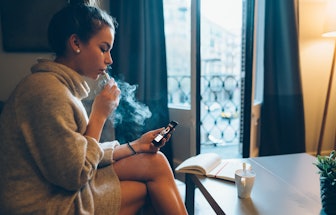 Young girl at home smoking electronic cigarette and online banking on mobile phone