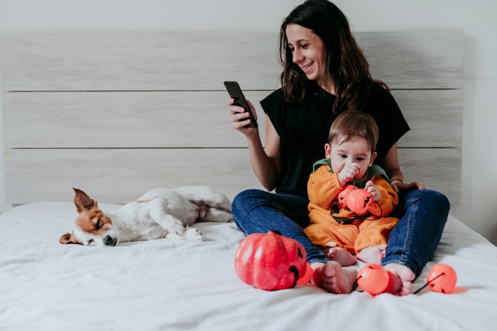 mom laughing at her phone with baby dressed as pumpkin