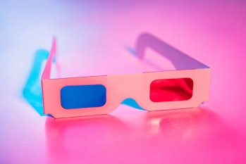 Aerial view of open retro 3d glasses with blue and red lens shadows on pink background
