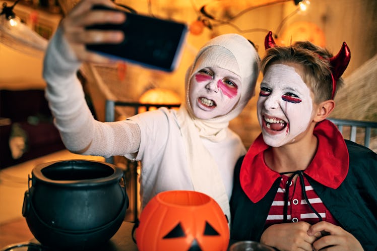 Two boys are taking selfies and posting a caption for mummy costumes at a Halloween party.