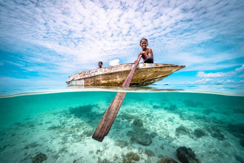 Split wide angle shot of Bajau Children rowing a wooden canoe in the ocean at a tropical island beac...