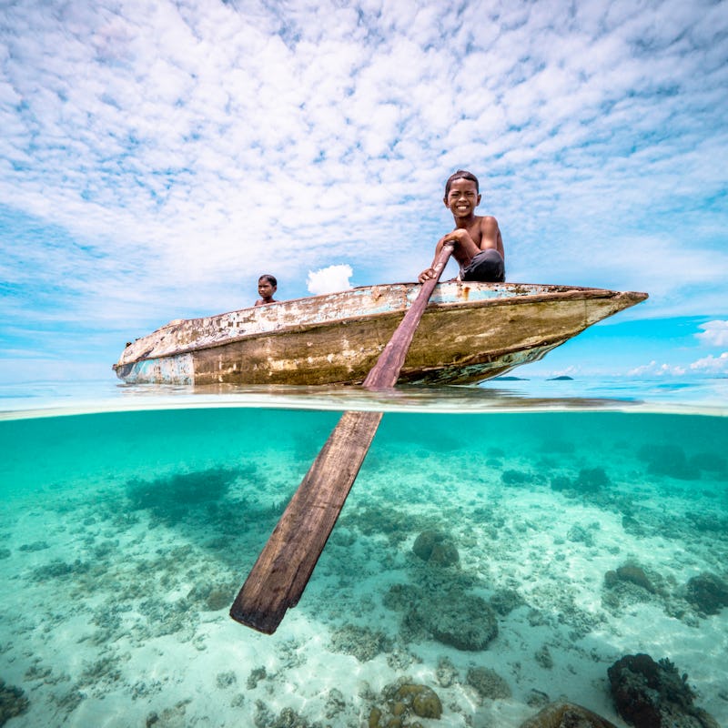 Split wide angle shot of Bajau Children rowing a wooden canoe in the ocean at a tropical island beac...