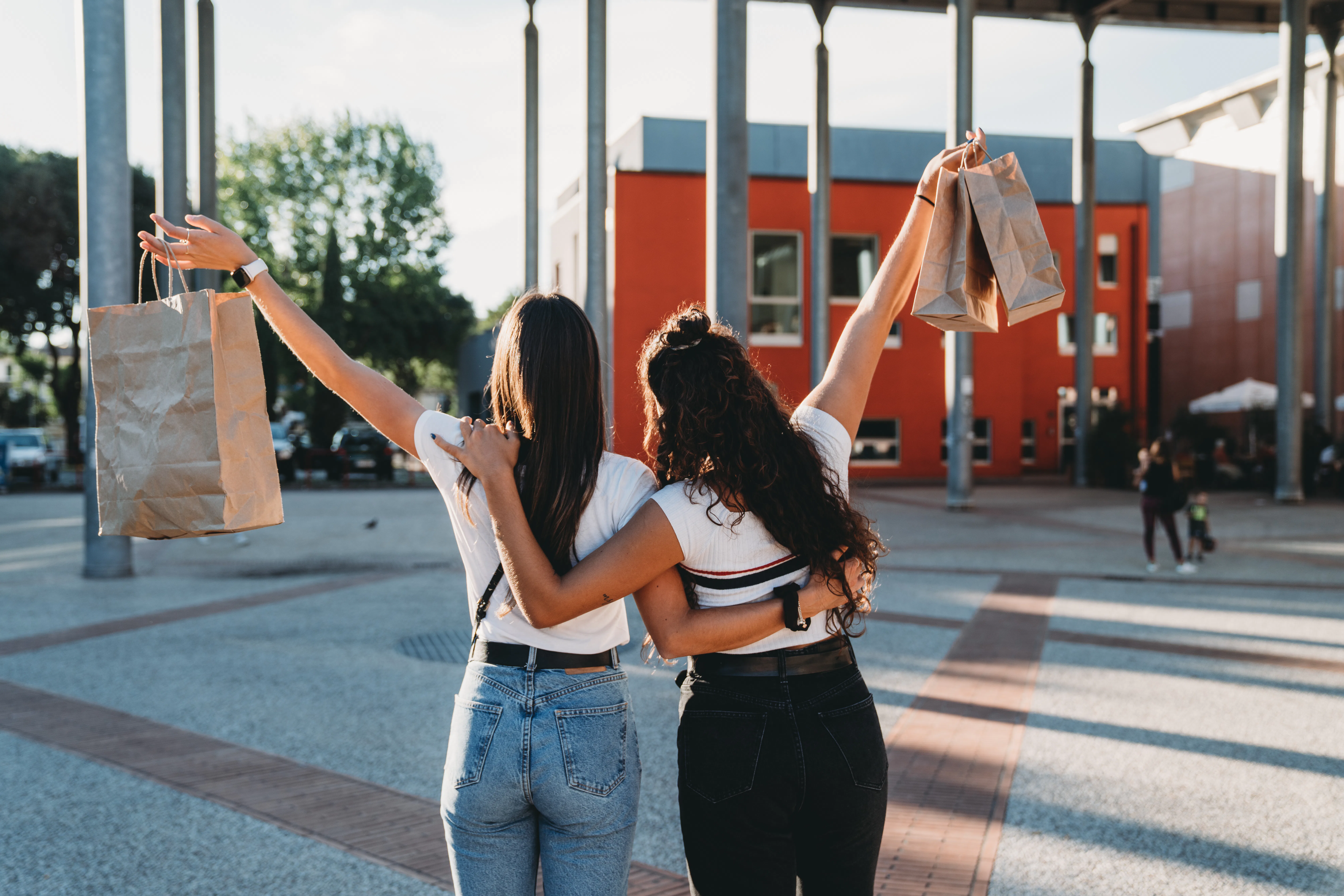 Two friends are shopping together in the city. Rear view of the friends embracing together.