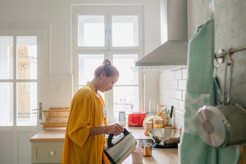 Photo of a mature woman making coffee in a kitchen of her apartment