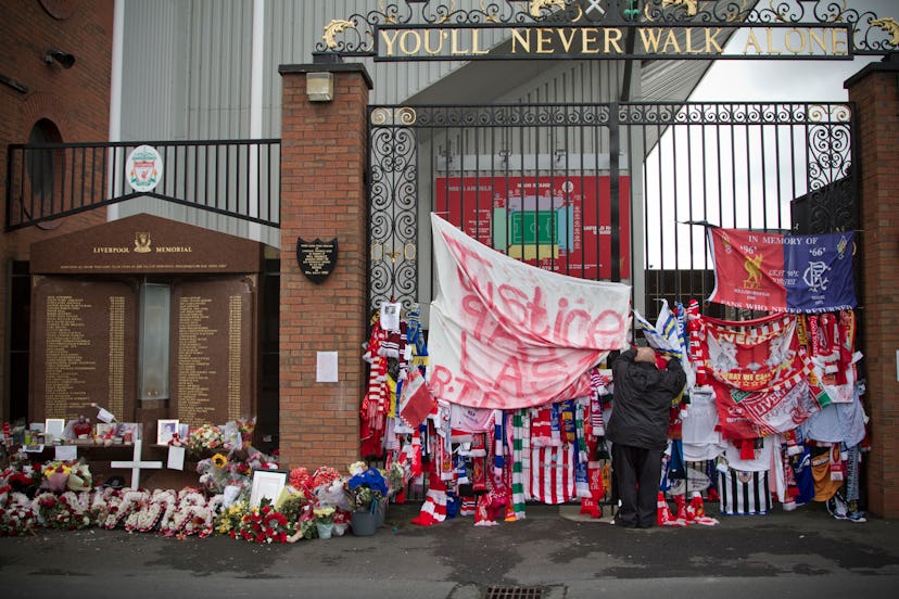 A man attaching a scarf to the Shankly Gates next to the memorial at Anfield to the 1989 Hillsboroug...