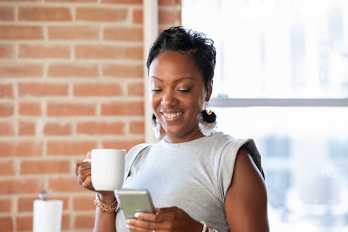 Woman holding cup of coffee while texting on smartphone