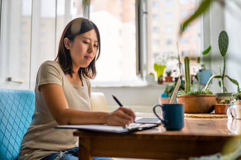 Young Asian woman working with laptop and writing notes at home
