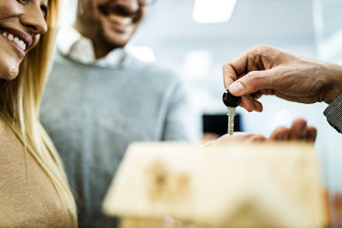 Close up of unrecognizable real estate agent giving home key to happy couple.