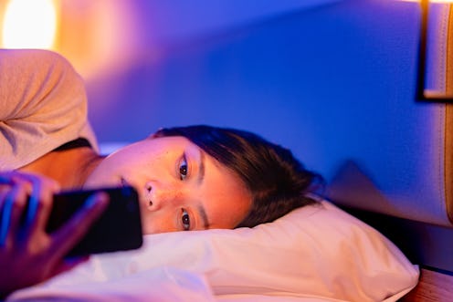 A young woman is using a smart phone in bed at night at home.