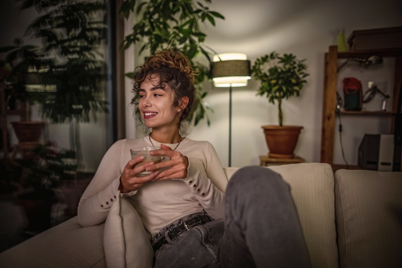 Shot of a young woman relaxing at night on sofa with a hot drink.