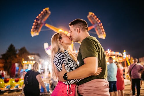 Young, loving heterosexual couple kissing in an amusement park.