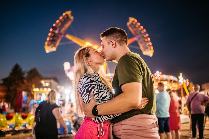 Young, loving heterosexual couple kissing in an amusement park.