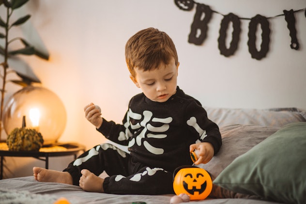 Baby boy playing on Halloween, sitting on bed and choosing candies.