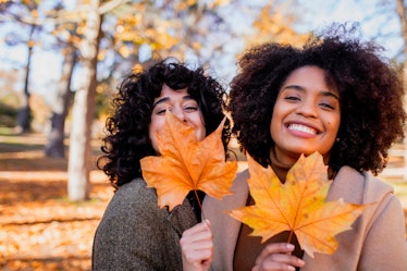 Young women holding autumn leaves, thinking about how their lucky zodiac signs will have the best Th...