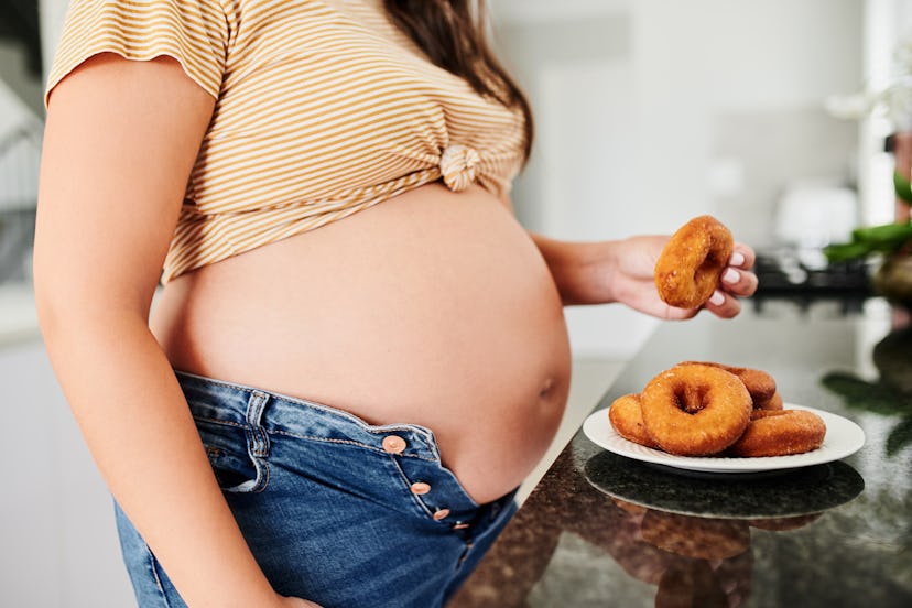 Shot of a pregnant woman snacking on donuts at home