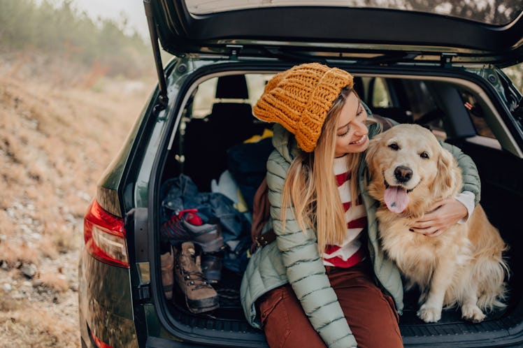 Photo of a young smiling woman and her dog sitting the trunk of a car on a beautiful autumn day, for...