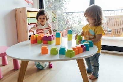 Front view of a little boy and a little girl playing with colorful plasctic toy blocks on a table at...