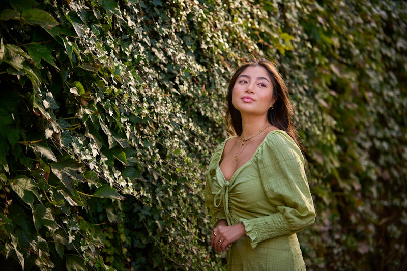 A woman wearing green stands in front of an ivy wall. The November 2021 new moon in Scorpio will fee...