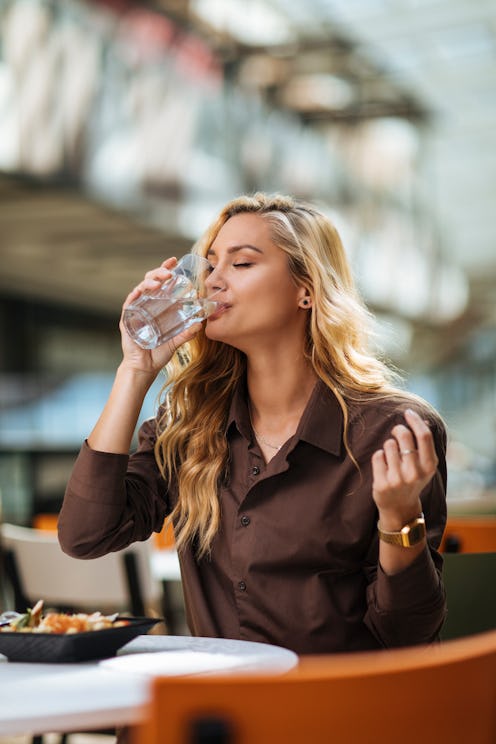 Beautiful young woman drinking water while having lunch at a shopping mall