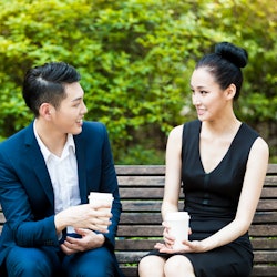 Two office colleagues are having a date outdoors in a park drinking coffee but it seems to be not th...