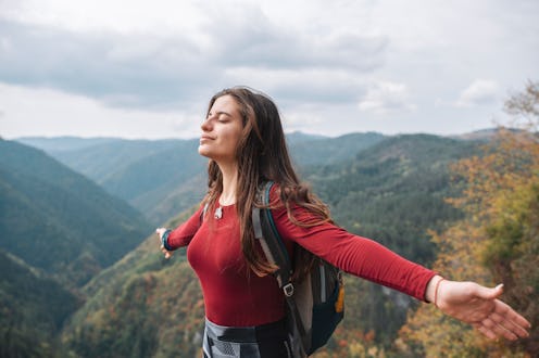 A woman stands at the top of a mountain. The November 2021 new moon will make these zodiac signs fee...