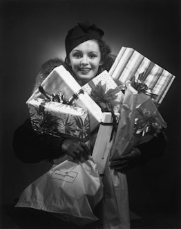 CIRCA 1955: A Christmas shopper, wearing a fur-trimmed coat and a winter hat, holding wrapped gift b...