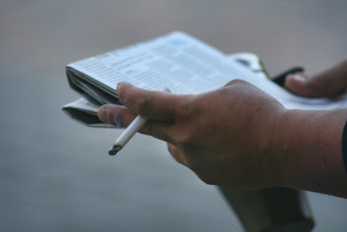 Man holding a lit cigarette while reading a newspaper in downtown Toronto, Ontario, Canada. (Photo b...