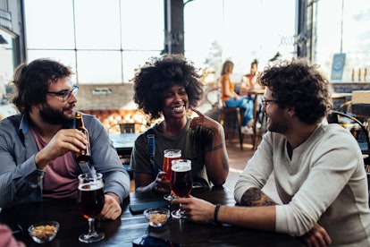 Four friends talking while drinking beer at a bar during the day