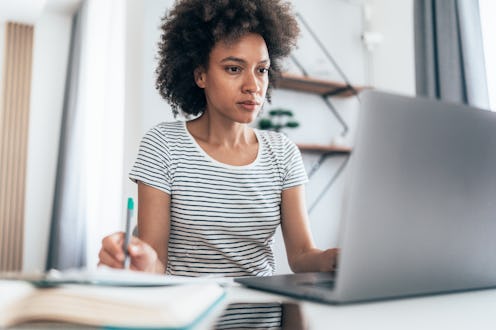 Young modern mixed race woman working from home, using laptop.