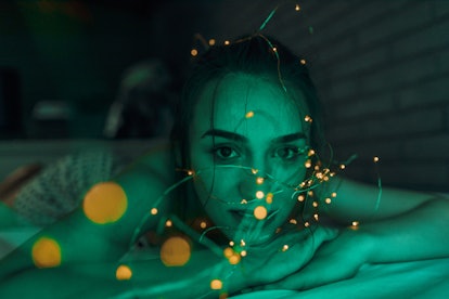 Young woman lying down on a bed in bedroom, tangled in fairy lights in December 2021, which will be ...