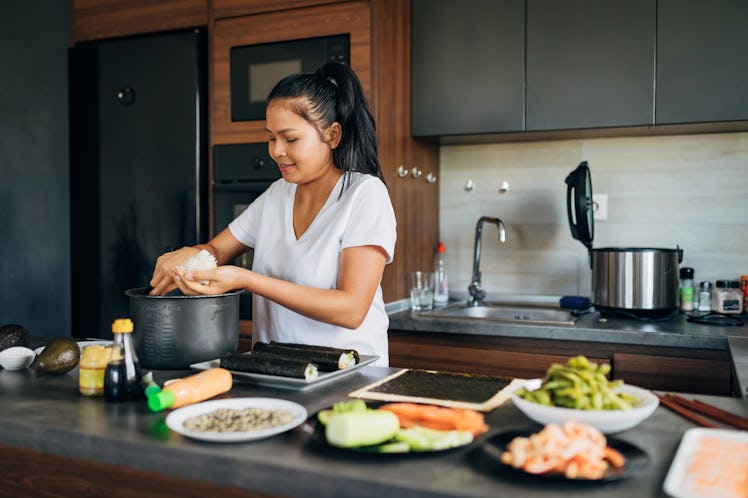 Skilled female sushi chef, making the rice balls for the Nigiri, in her modern domestic kitchen
