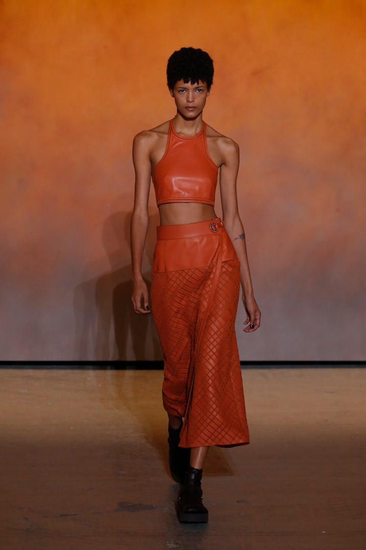 A model walking in an orange top and pants at the Hermes Ready to Wear Spring/Summer 2022 fashion sh...