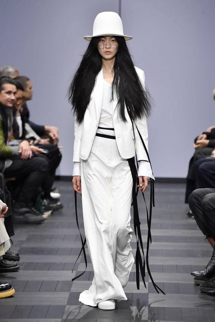 A model walking in a white suit and hat at the Ann Demeulemeester Ready to Wear Spring/Summer 2022 f...