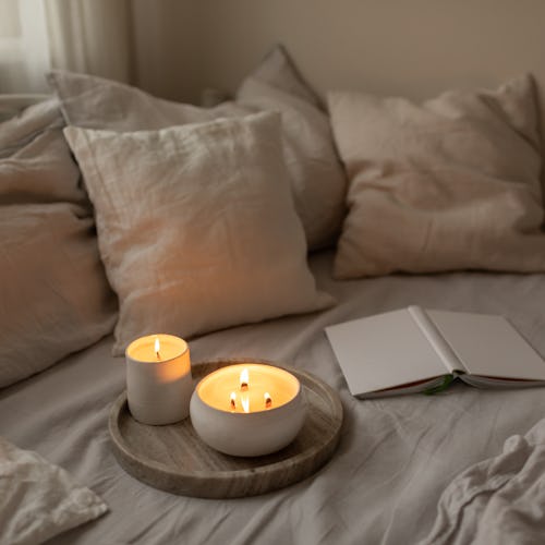 Organic soya wax candles with wooden candlewick in white ceramic bowls on linen bedding set with boo...