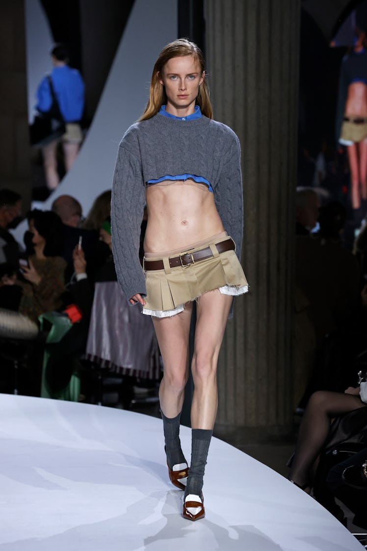 A model walking in a grey crop sweater and beige mini skirt at the Miu Miu Womenswear Spring/Summer ...
