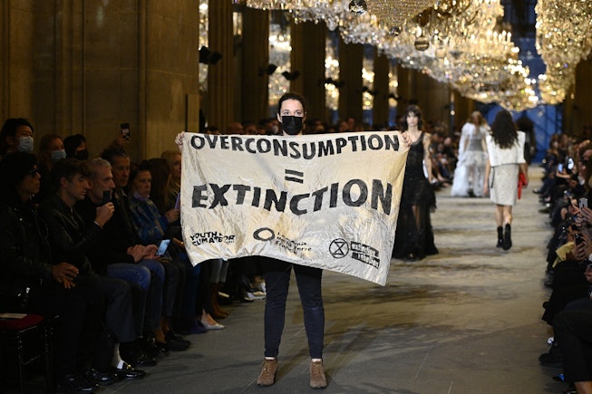 A demonstrator holds a banner as models present creations by Louis Vuitton during the Women's Spring...