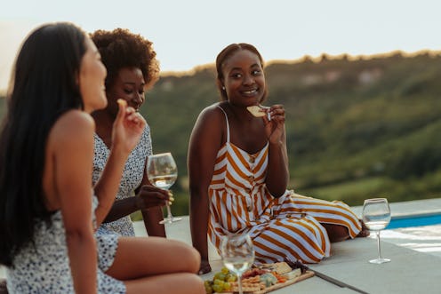 Multiracial female friends at picnic by the pool drinking wine